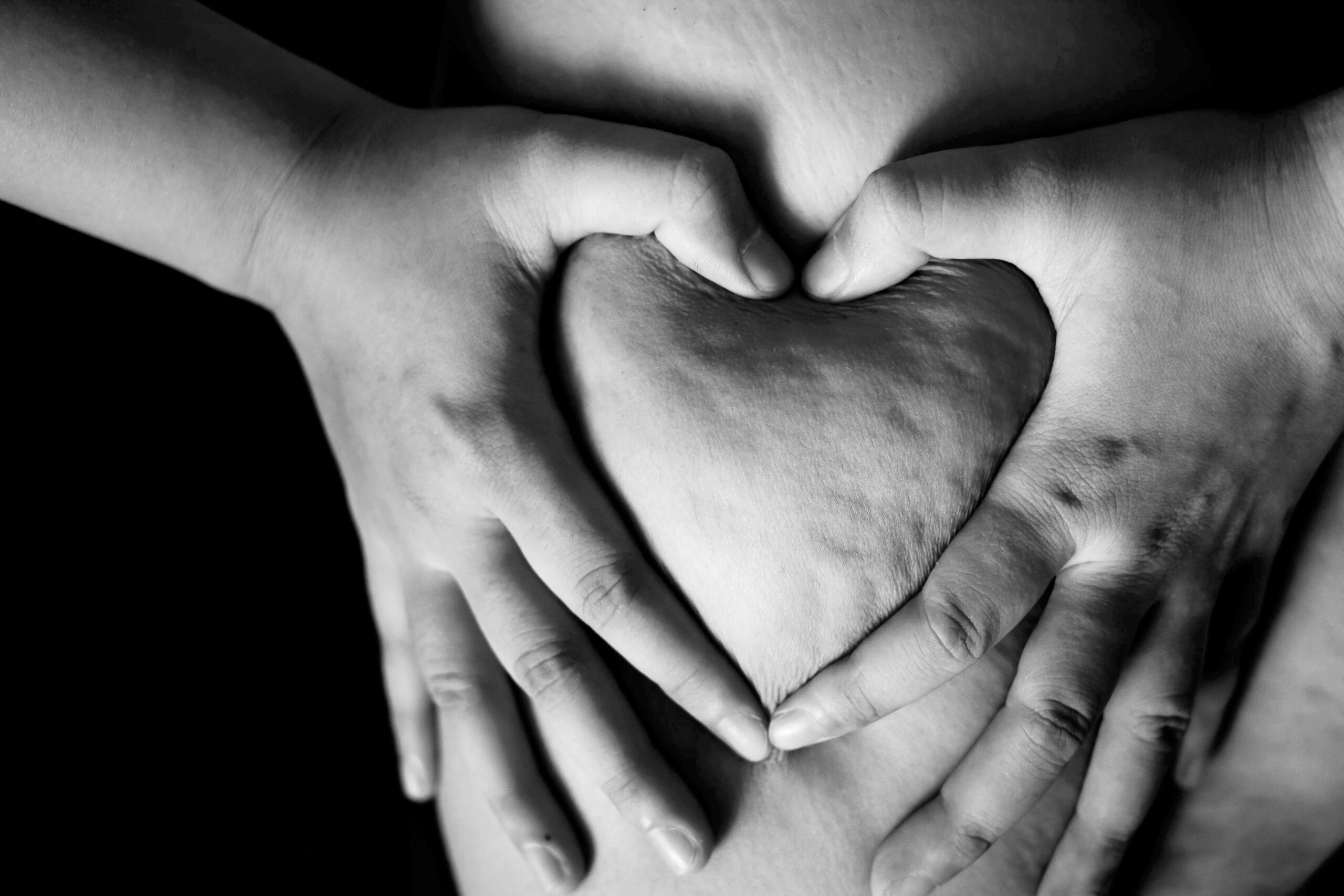 A black and white photo showing a person making a heart shape out of their flesh with their hands.