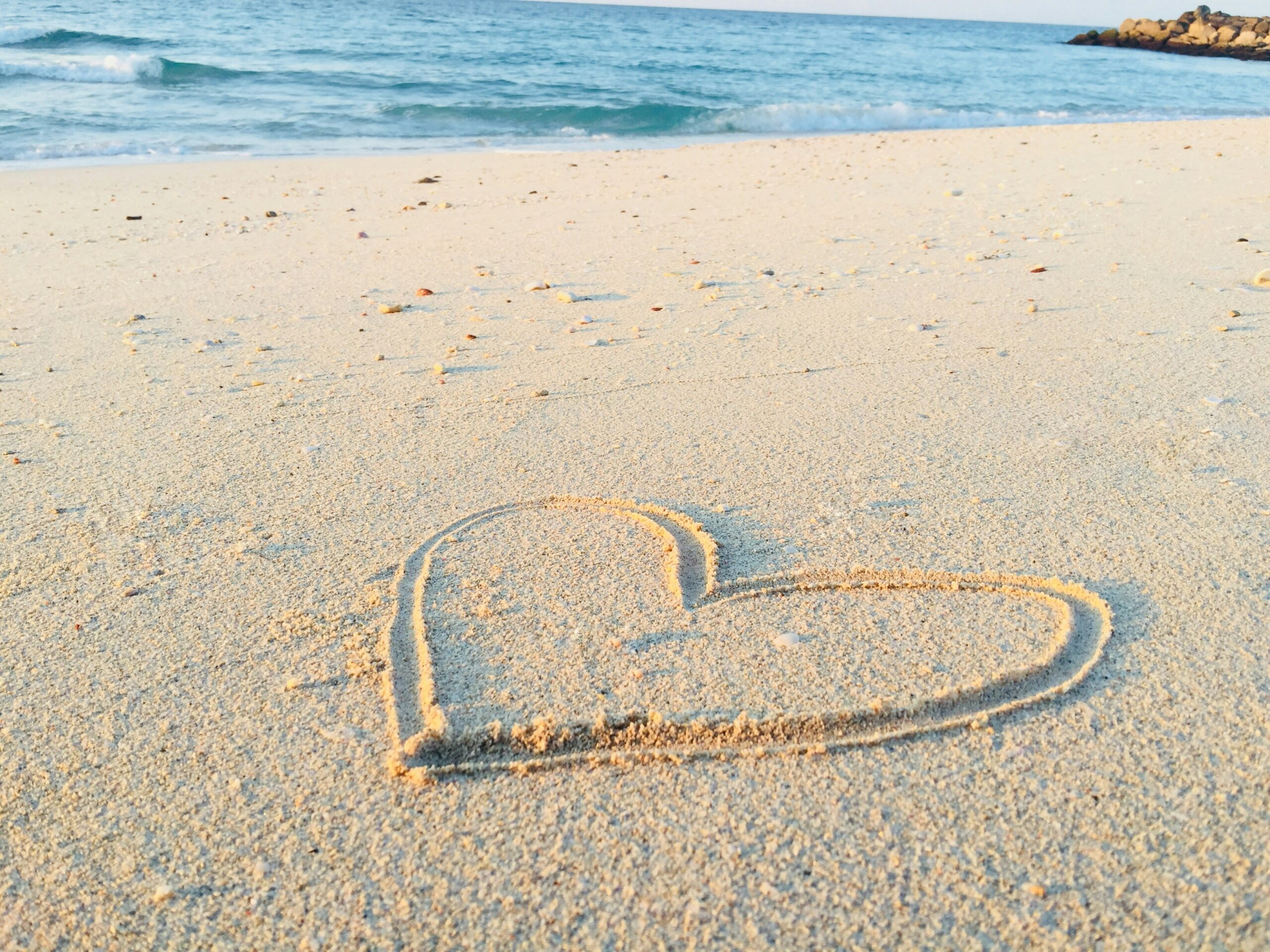 Photo of sand with a bit of sea and a big heart drawn in the sand