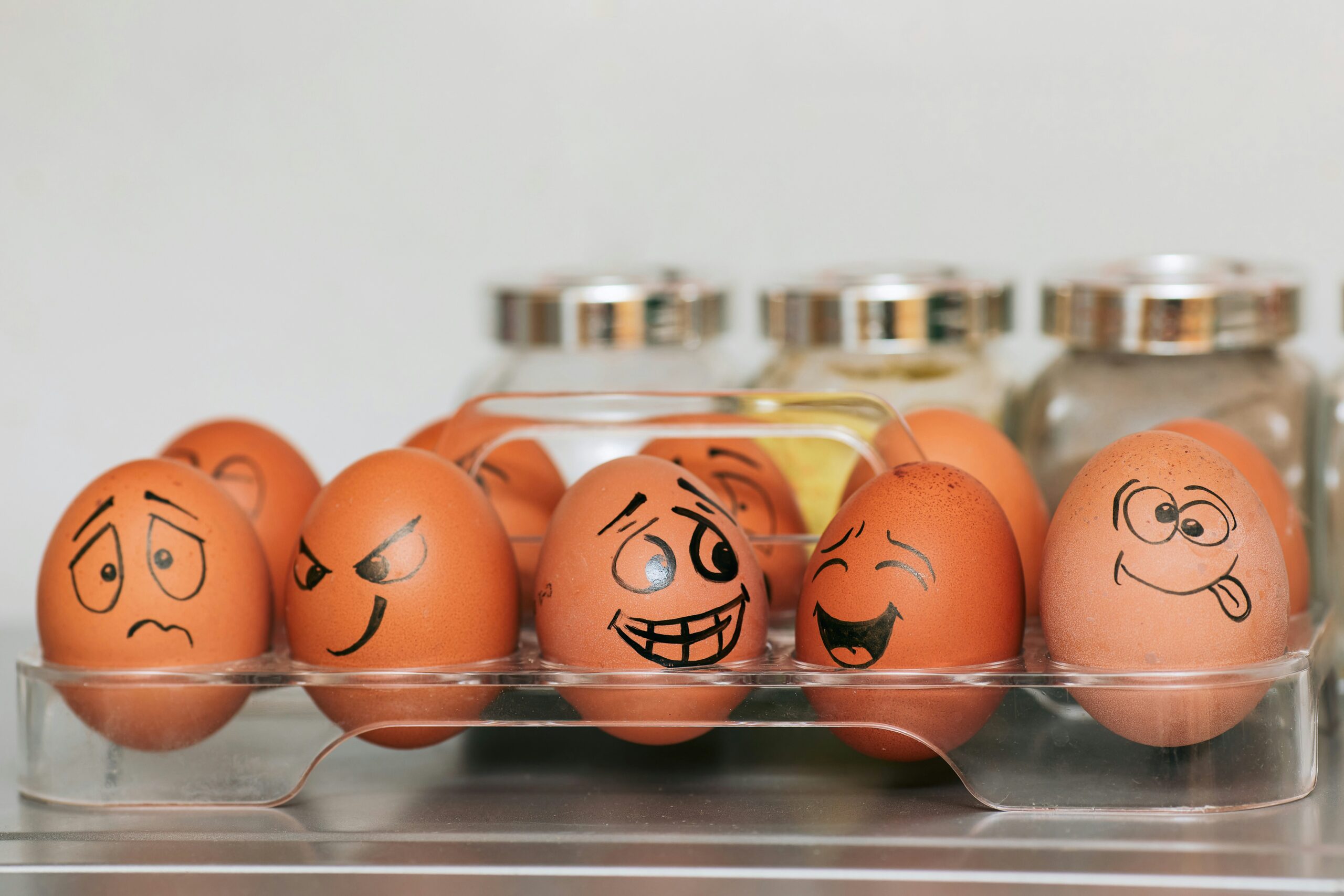 This picture shows and egg box in a kitchen and the eggs each have different emotions drawn on their faces