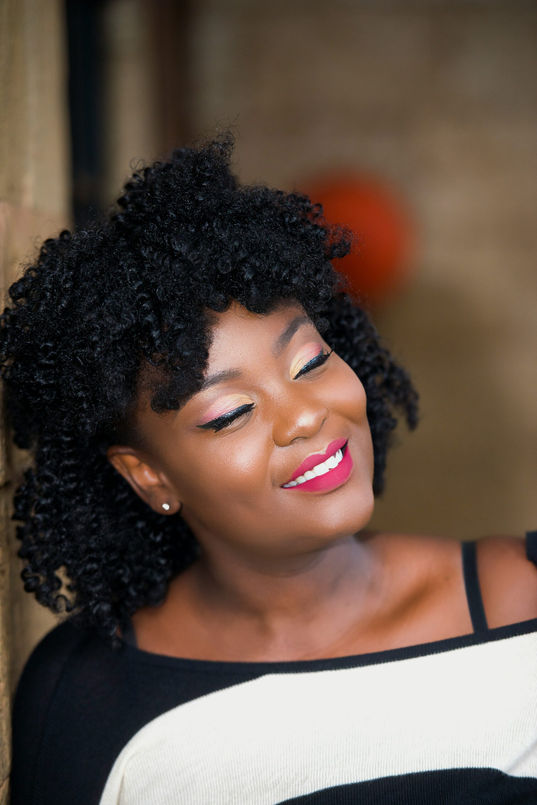 Image of a radiant woman wearing a black and white jumper looking to the right wearing bright pink lipstick