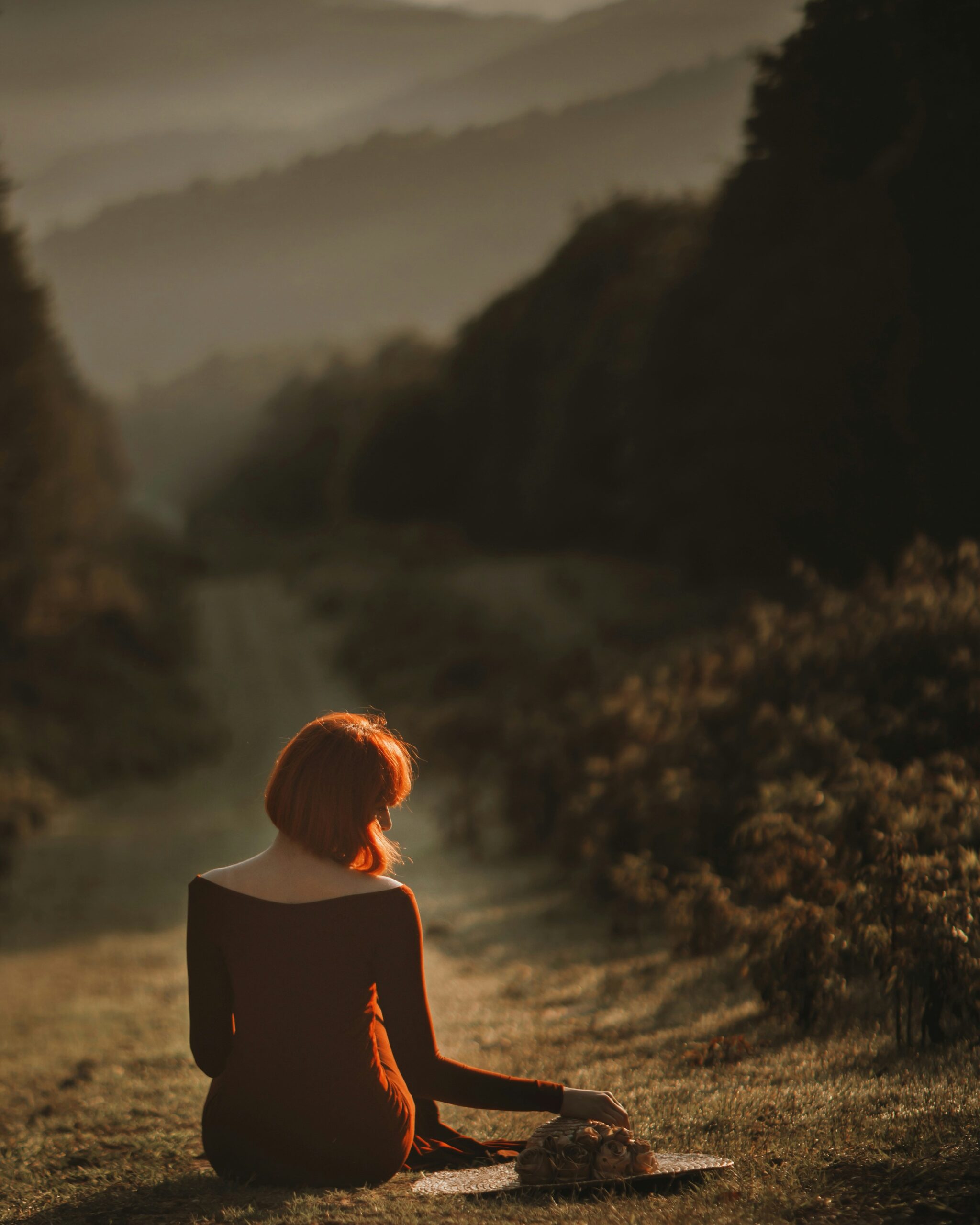 A woman sits on a forest pathway, gazing into the distance, embodying a moment of reflection and inner peace.