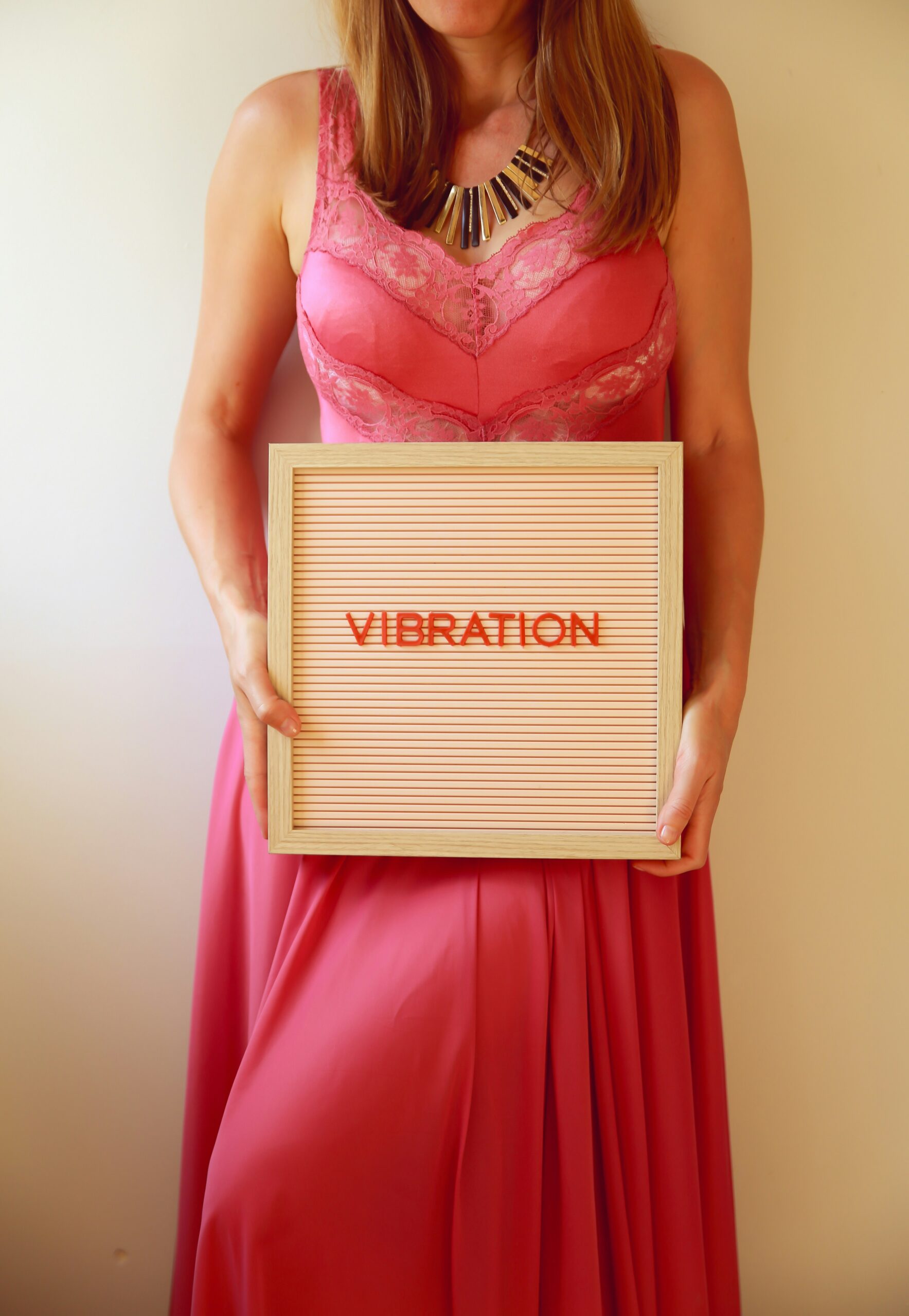 Woman in a long pink lacy nightie holding a “Vibration” sign, radiating joy, alignment, and the magnetic energy of abundance and manifestation.