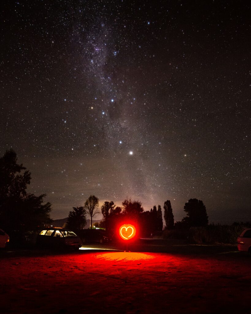 People in a car gazing at a glowing neon heart under a starry sky, symbolising heart expansion and spiritual connection.