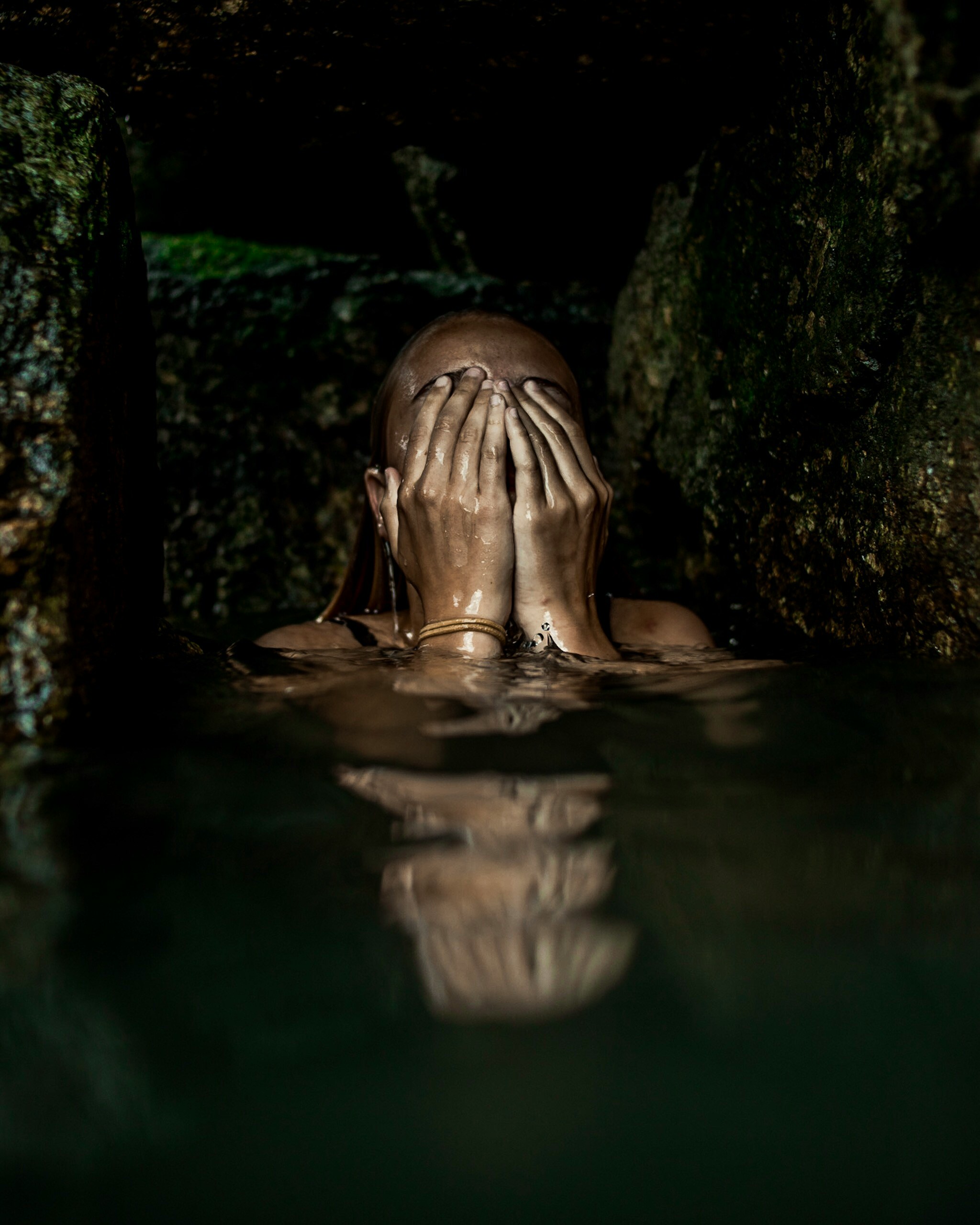 A woman in water with her face covered by both hands, evoking vulnerability and introspection.