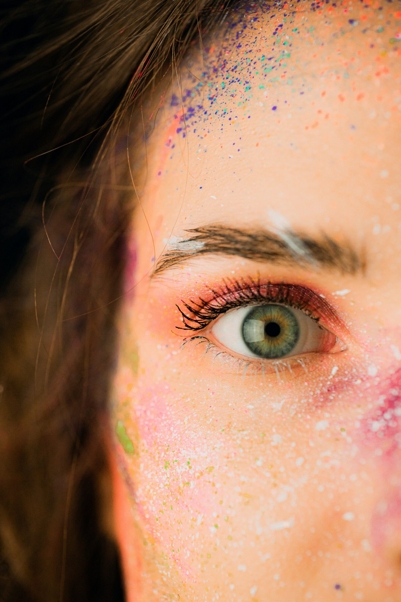 Woman with green eyes and colourful paint on the right side of her face, symbolising creative expression, radiance, and the power of manifestation.